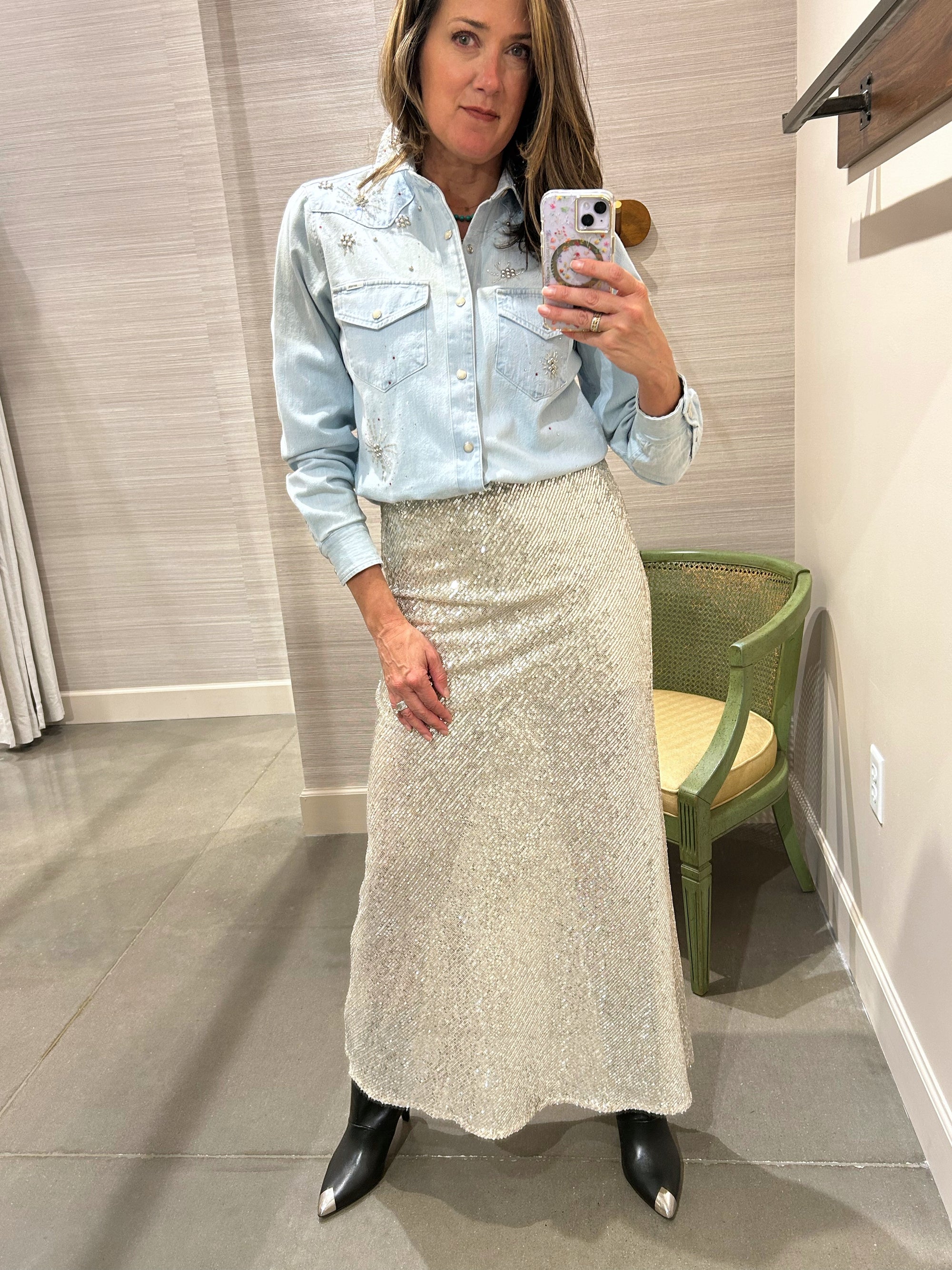 Woman taking a mirror selfie wearing a light blue denim shirt and silver sequin skirt.